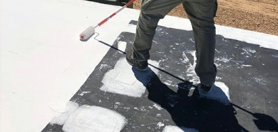 Roofer rolling asphalt roof coating onto a commercial flat roof