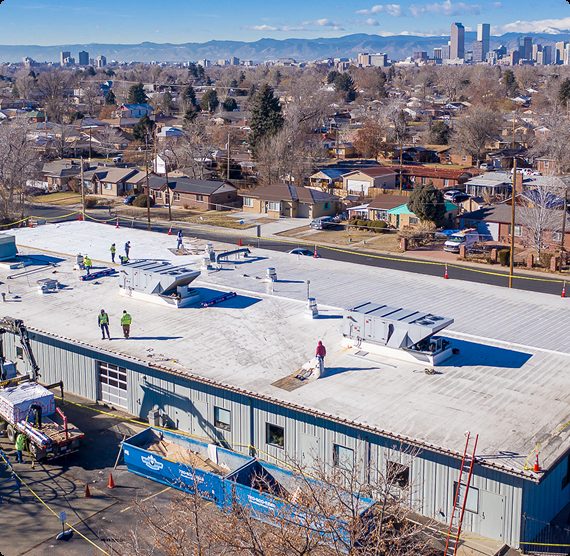 Aerial view of a commercial flat roof replacement in progress with the Denver skyline and surrounding neighborhood in the background