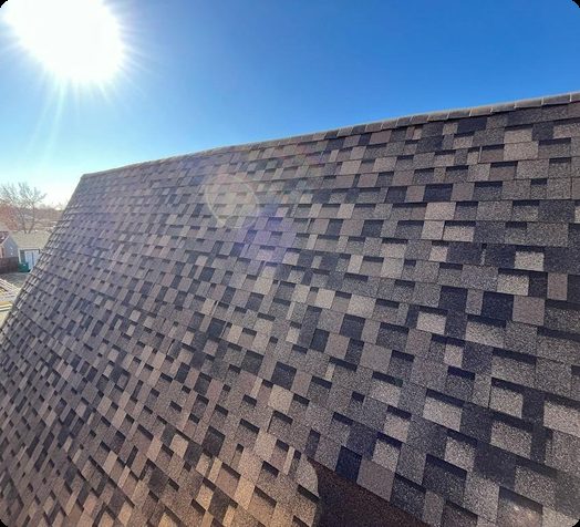 Close-up view of a dark asphalt shingle roof on a sunny day
