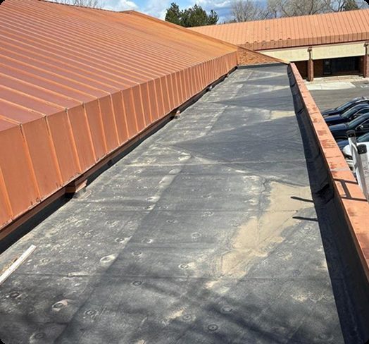 Flat roof membrane section next to a copper-toned metal standing seam roof