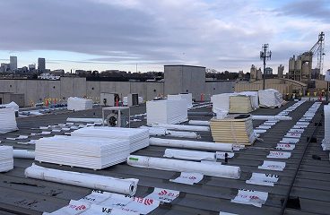 Insulation boards and membrane rolls staged on a commercial rooftop with a city skyline in the background