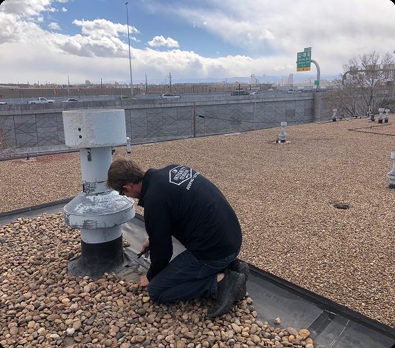 Roofer repairing flashing around an HVAC curb on a gravel-ballasted commercial roof