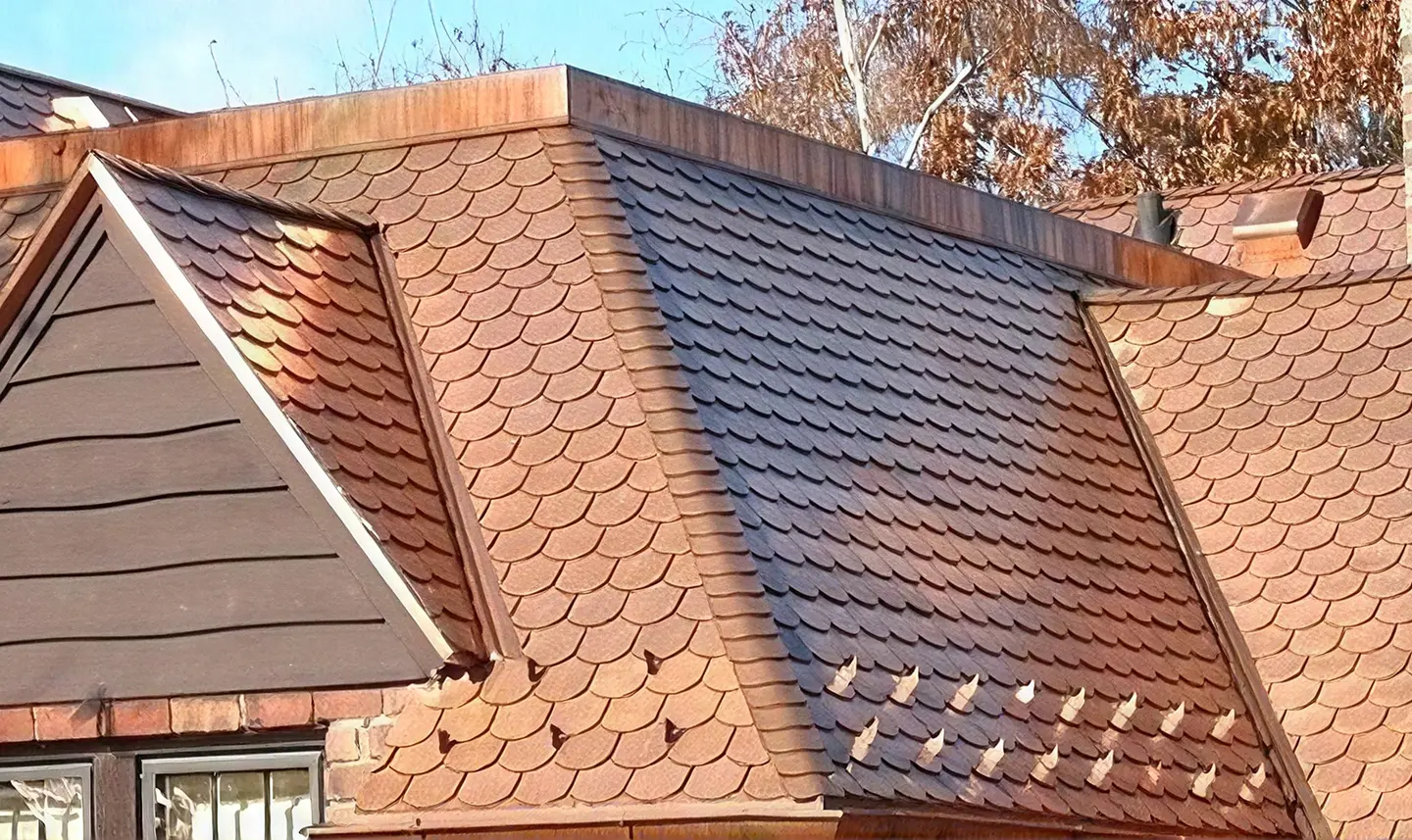 Close-up of a scalloped clay tile roof with a contrasting dark shingle section and copper ridge flashing