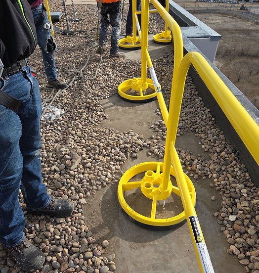 Close-up of a yellow guardrail's circular weighted base on a rooftop during installation