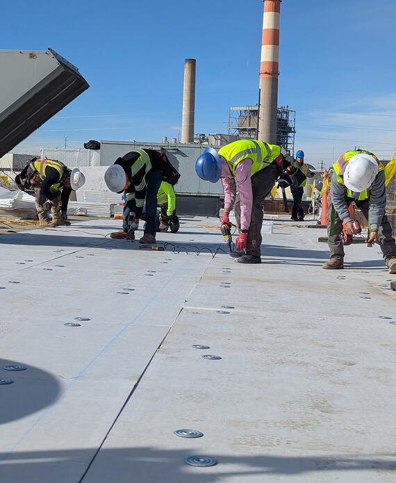 Roofing crew in hard hats and high-visibility vests fastening insulation board on an industrial commercial roof