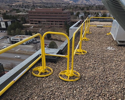 Yellow non-penetrating guardrail system with weighted bases installed along a commercial rooftop edge