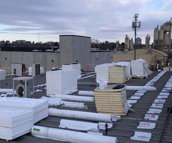 Rolls of TPO membrane, polyiso insulation boards, and cover board staged on a commercial rooftop