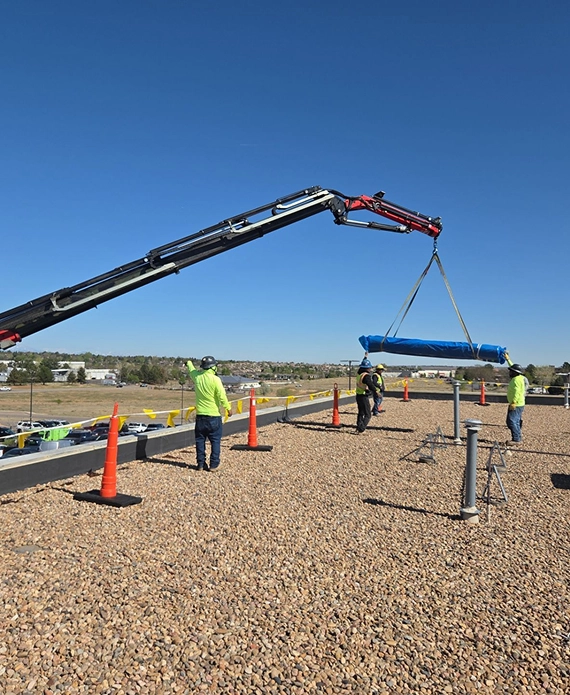 Roofing crew in safety gear guiding a crane lifting materials onto a gravel ballasted commercial rooftop