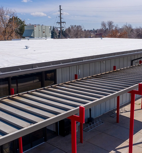 Completed white TPO membrane roof on a commercial building with a red-column metal canopy below